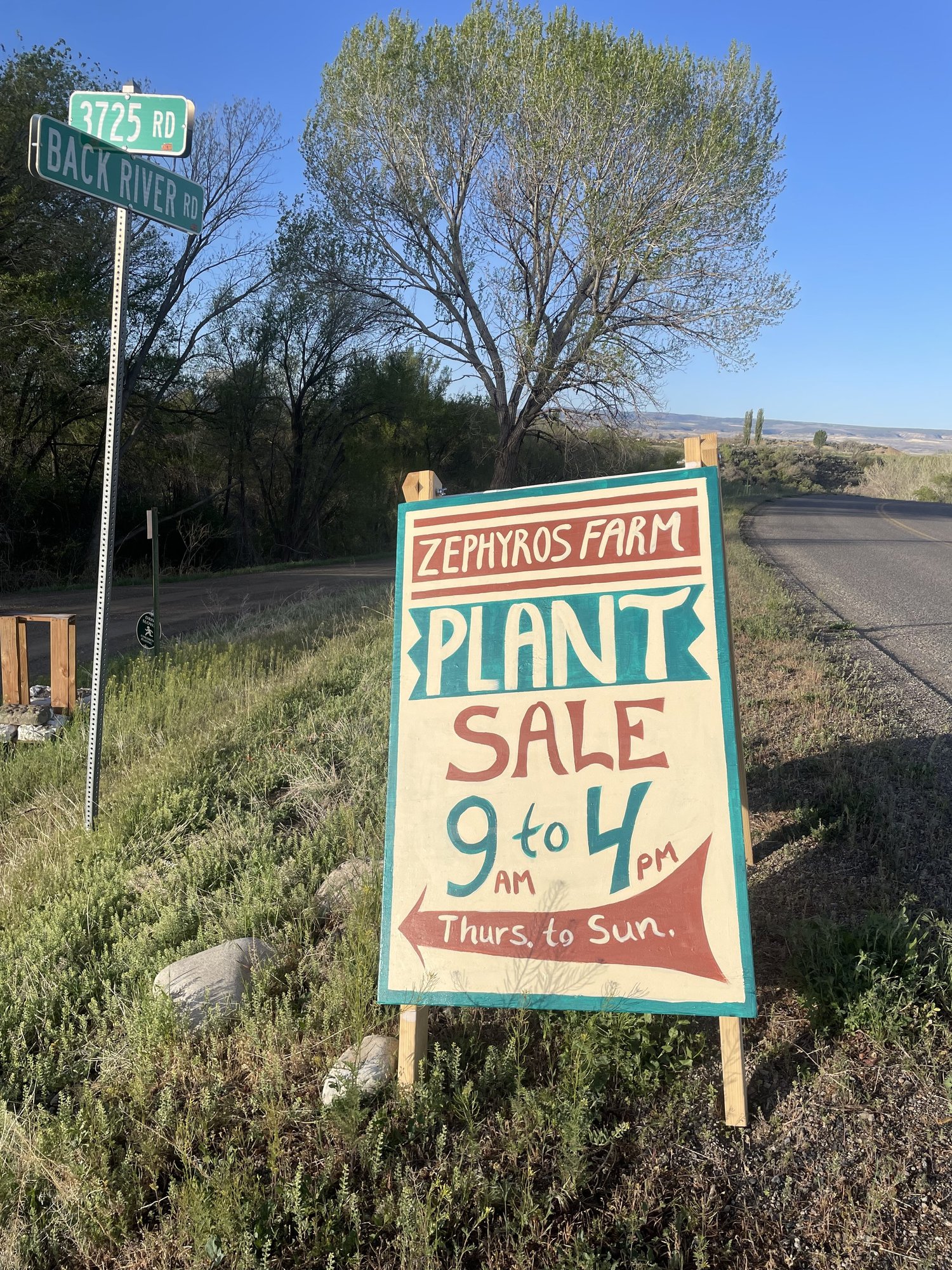Sign for Zephyros Farm plant sale located at the intersection of Back River Road and 3725 Road, open from 9 AM to 4 PM, Thursday to Sunday.